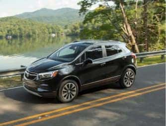 A Buick-GMC SUV driving on the road, near a lake
