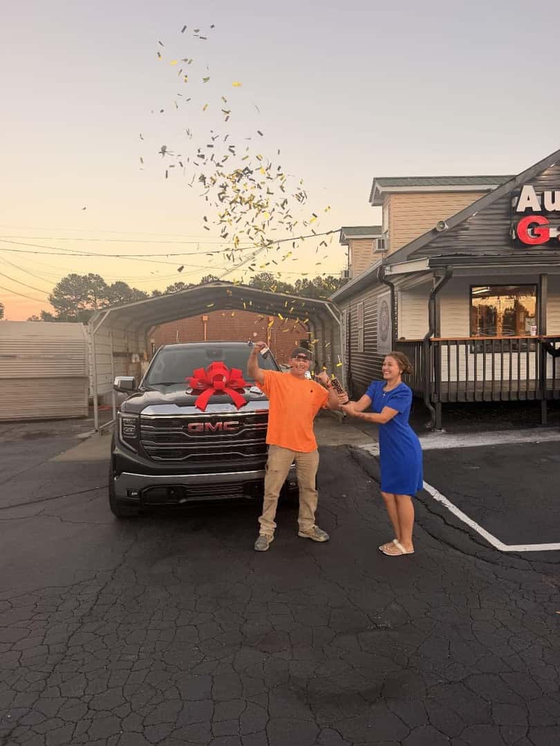 Customers celebrating beside a GMC SUV with a red bow at Auto Gallery
