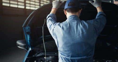 Person looking under the hood of a car from behind