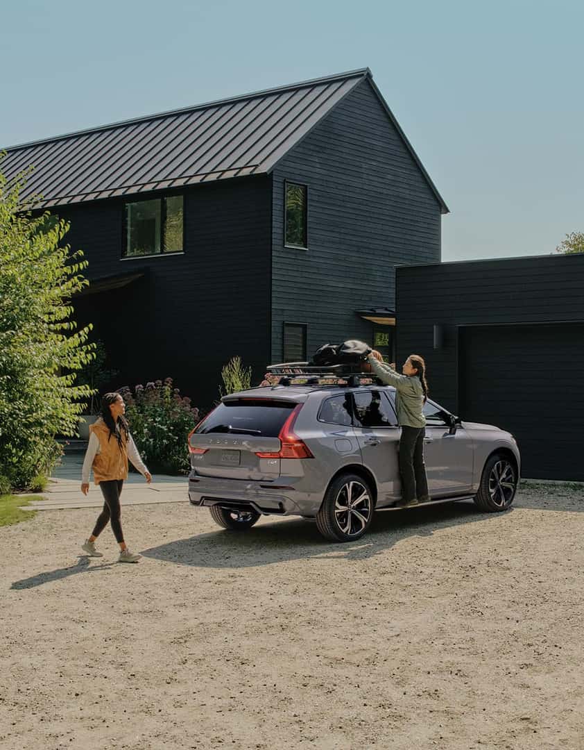 2026 Volvo XC60 | Gray Volvo XC60 Parked in Driveway Outside of Black House While Two Women Pack Roof Rack On Vehicle