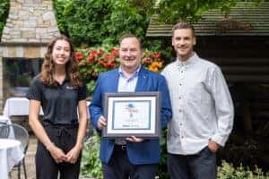 Three people standing next to each other. One in the middle holding best patio plaque