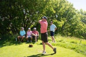 Man swinging golf club while four people are watching 