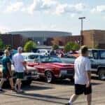 People walking by a red car and brown car at car cruise