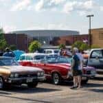 People standing in front of red car and brown car at car show
