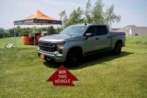 gray 2025 Chevrolet Silverado 1500 with "Win this Vehicle" sign in front of it at hole in one golf event