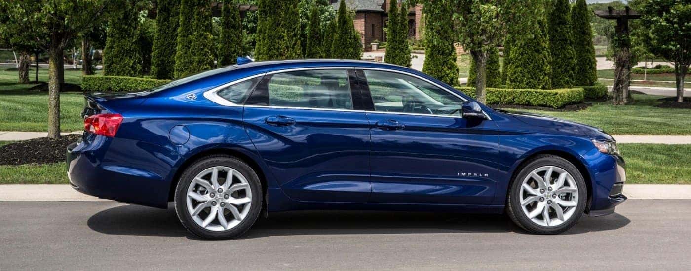 A blue 2018 Chevy Impala is shown on a tree-lined road after visiting a used car dealer.