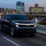 A black 2025 Chevy Silverado EV RST is shown driving on a bridge.