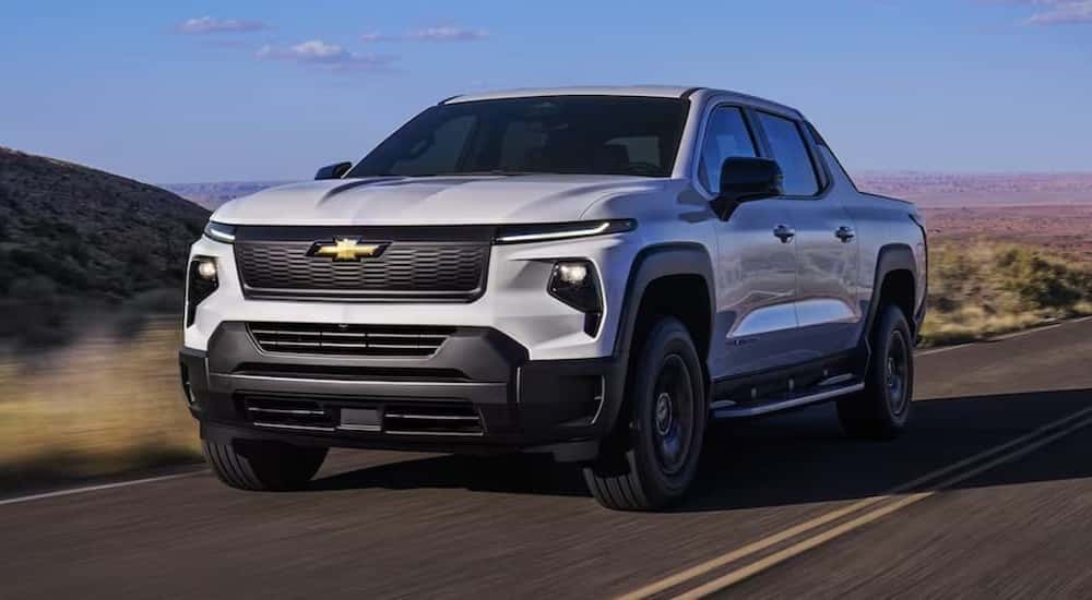 A white 2025 Chevy Silverado EV for sale is shown driving on a highway.