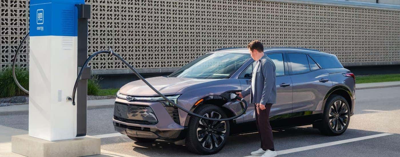 A man charging a grey 2024 Chevy Blazer EV parked by a charging station.