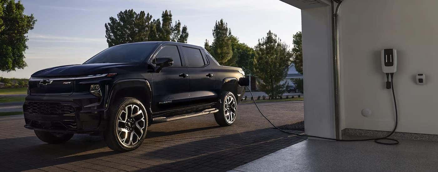 A black 2024 Chevy Silverado EV plugged into a home charging station.