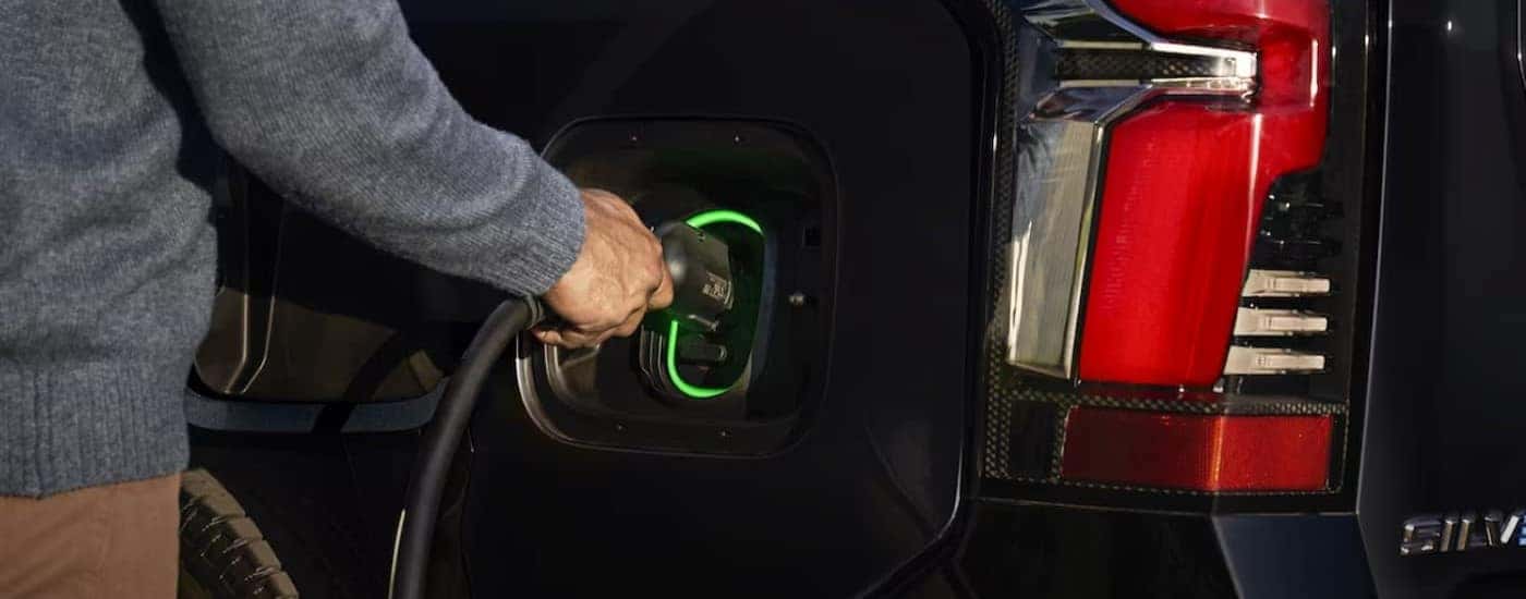 A person is shown charging a black 2024 Chevy Silverado EV for sale near Winston-Salem.