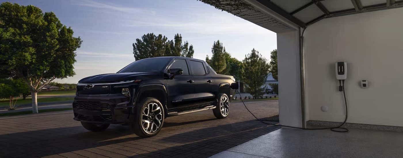 A black 2025 Chevy Silverado EV charging outside of a garage.