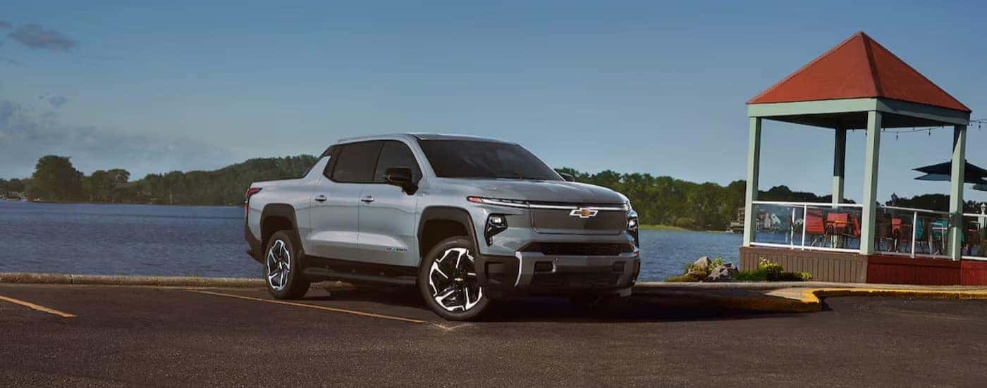 A silver 2024 Chevy Silverado EV is shown parked near a lake.