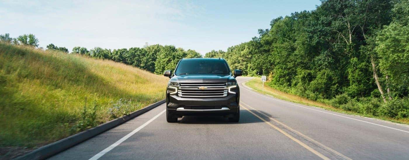 A grey 2021 Chevy Tahoe High Country driving on a tree-lined road.