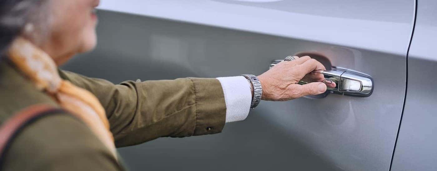 A person opening the door on a silver 2023 Chevy Traverse.