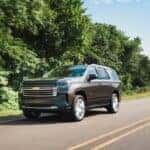 A grey 2021 used Chevy Tahoe High Country for sale driving on a tree-line road.