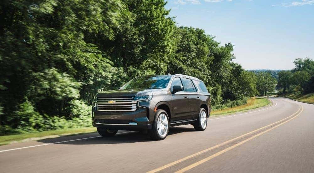 A grey 2021 used Chevy Tahoe High Country for sale driving on a tree-line road.