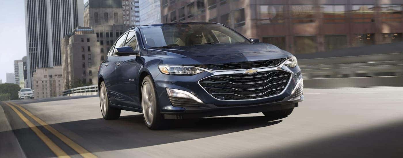 A dark blue used 2022 Chevy Malibu driving down a city street