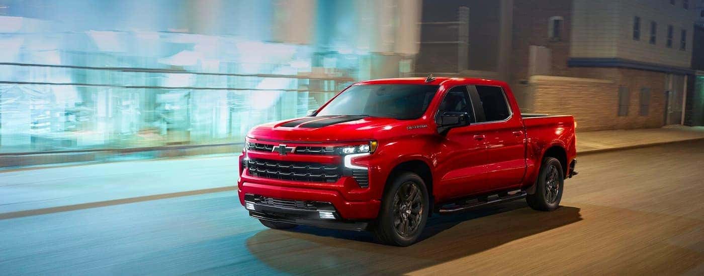 A red 2023 Chevy Silverado 1500 RST driving in a city.