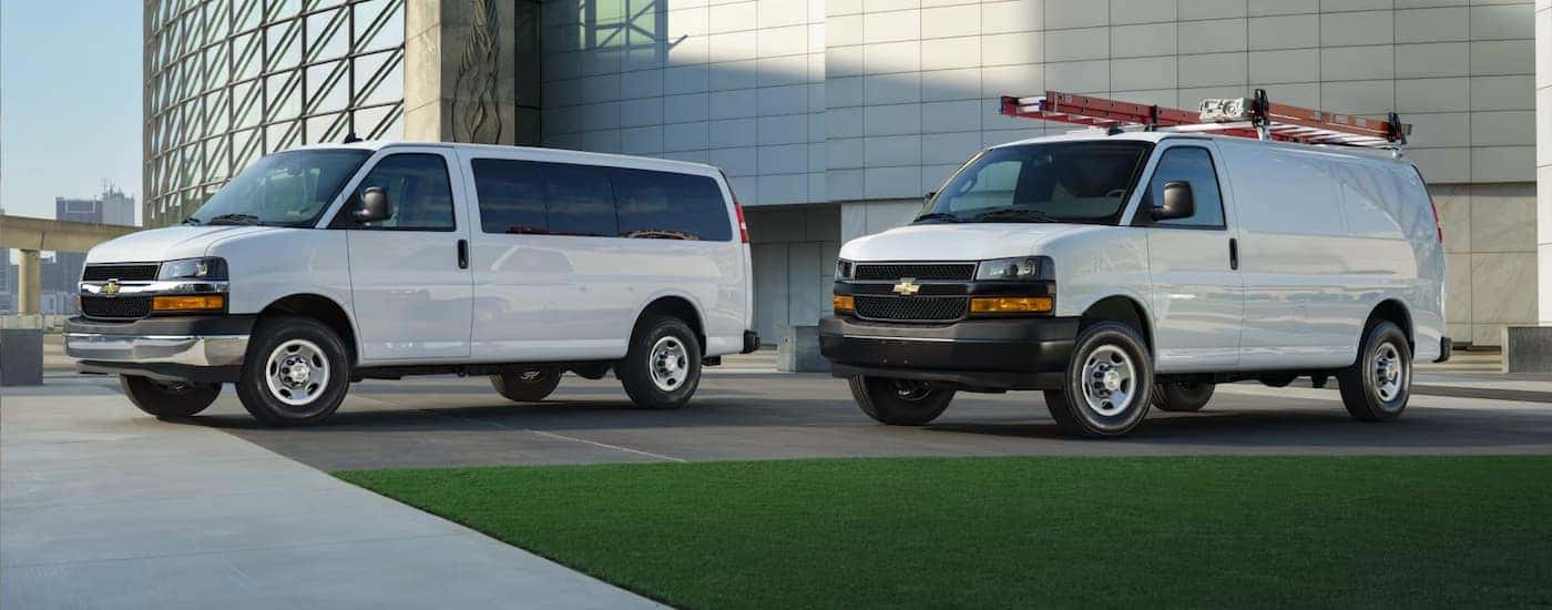 Two white 2026 Chevy Commercial Vans parked at a jobsite