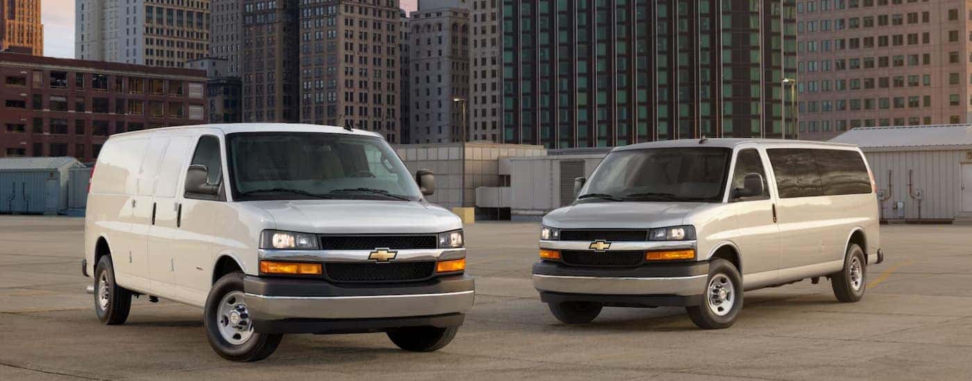 Two white 2026 Chevy Express Vans parked in a city