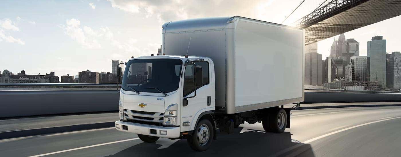 A white 2026 Chevy Low Cab Forward commercial truck driving in a city