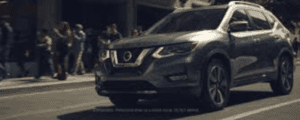 Grey Nissan Rogue with silver rims on street with poeple nearby on sidewalk