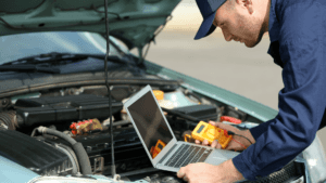 close up of vehicle mechaninc holding laptop over vehicle hood running diagnostic testing