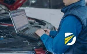 close up of vehicle mechanic working on computer running diagnostic testing with vehicle hood up
