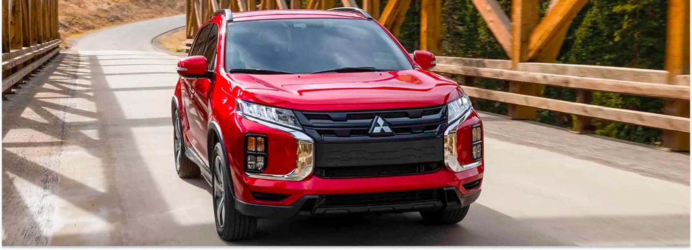Red 2026 Mitsubishi Outlander Sport driving across a wooden bridge outdoors.