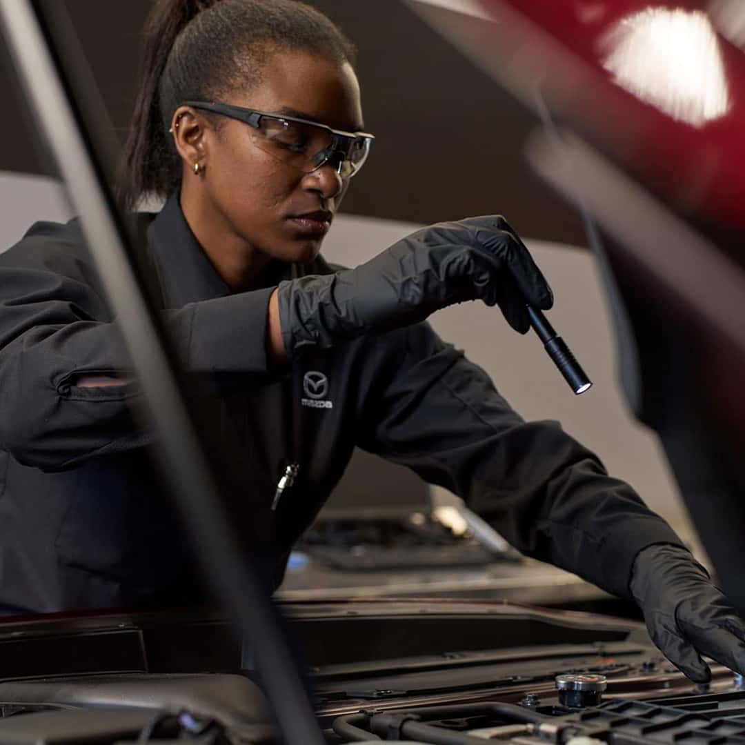 Technician looking at the hood of a car holding a flashlight