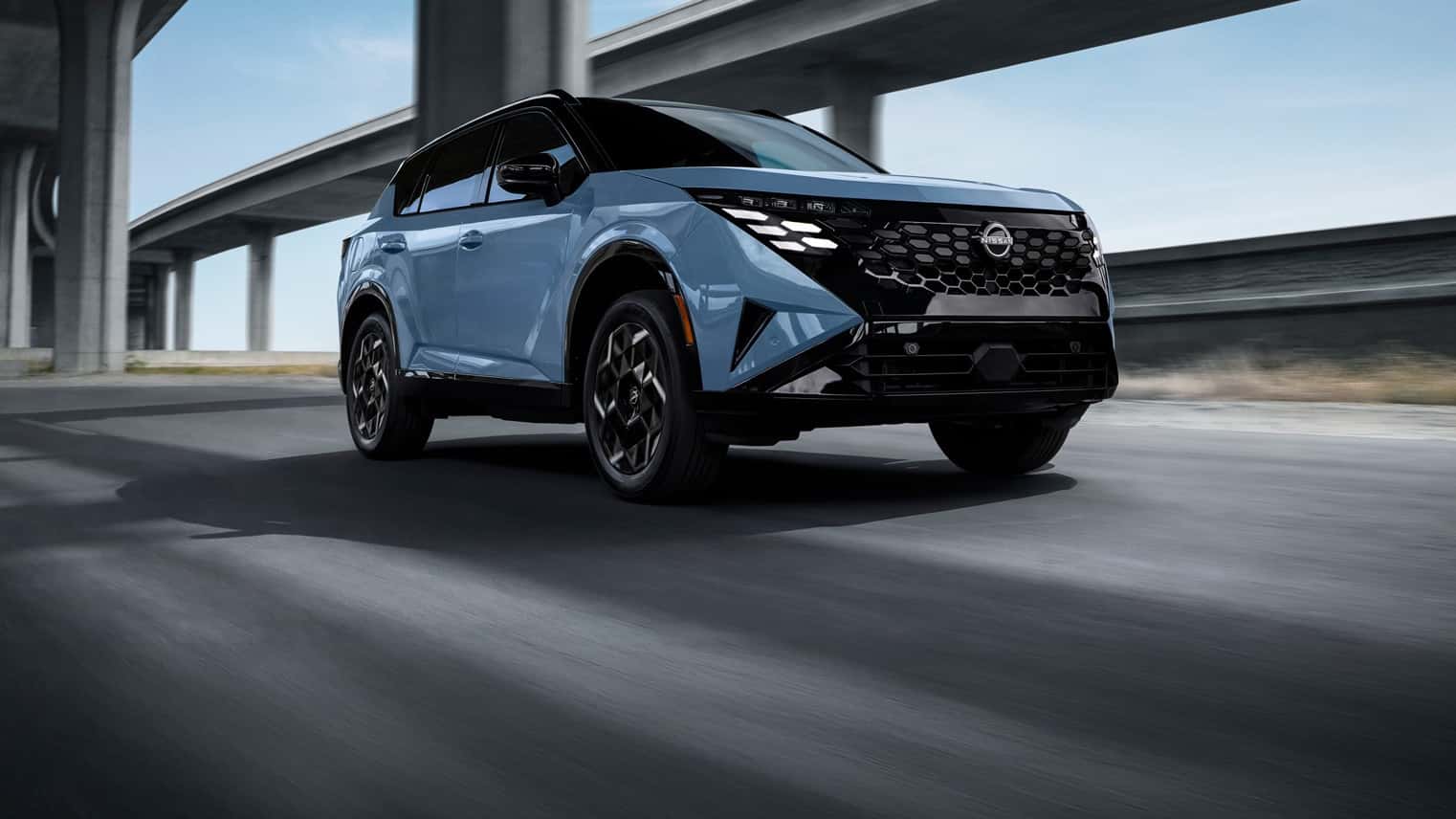 The all-new 2027 Nissan Rogue Hybrid in Horizon Blue Pearl Metallic with a black roof and gloss black honeycomb grille, driving under a highway overpass